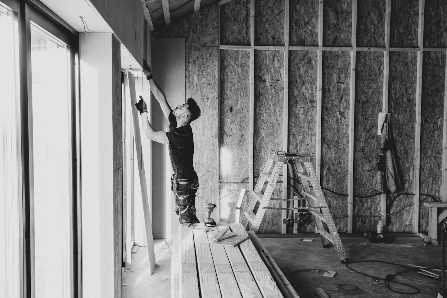 Un uomo installa un pannello di cartongesso su un muro in un edificio.