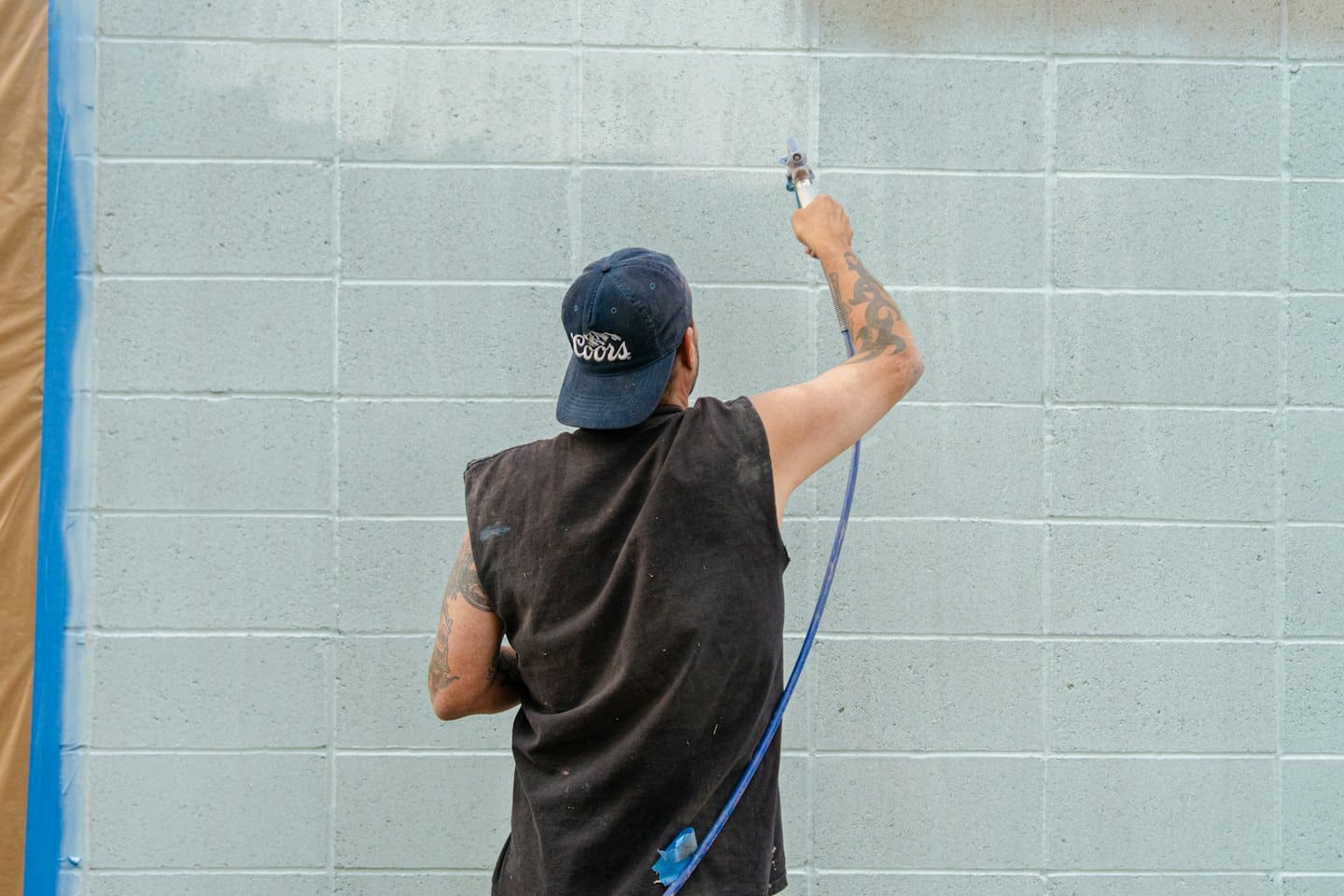 Un operaio edile vernicia a spruzzo un muro di blocchi di cemento.