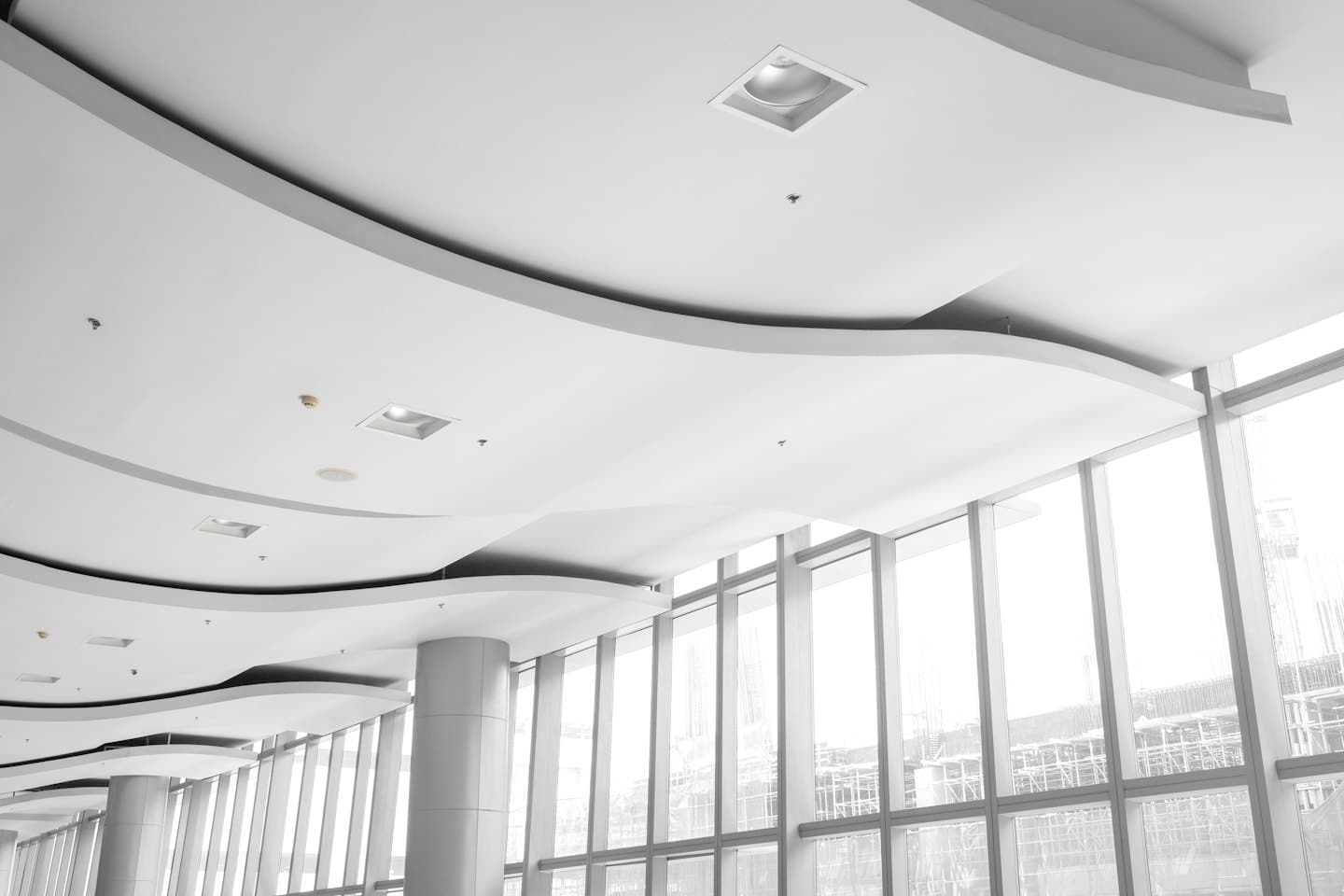 Soffitto moderno di un ufficio bianco con pannelli curvi e grandi finestre.