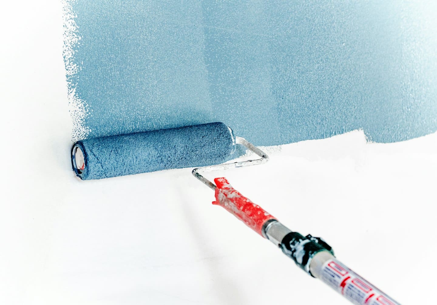 Rullo da pittura che applica vernice azzurra a una parete bianca.