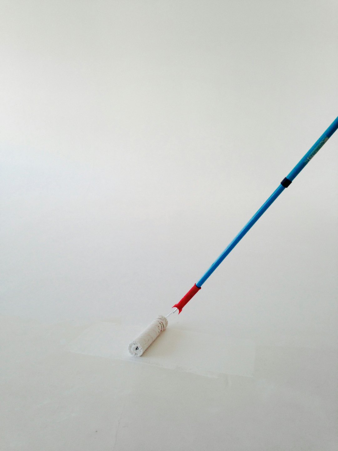 Pittura una parete con un rullo manico blu e rosso.